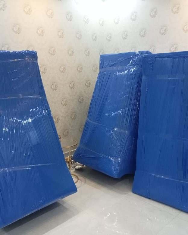 ثلاث قطع أثاث كبيرة مغلفة بالنايلون الأزرق ومربوطة بالشريط قبل تحميلها